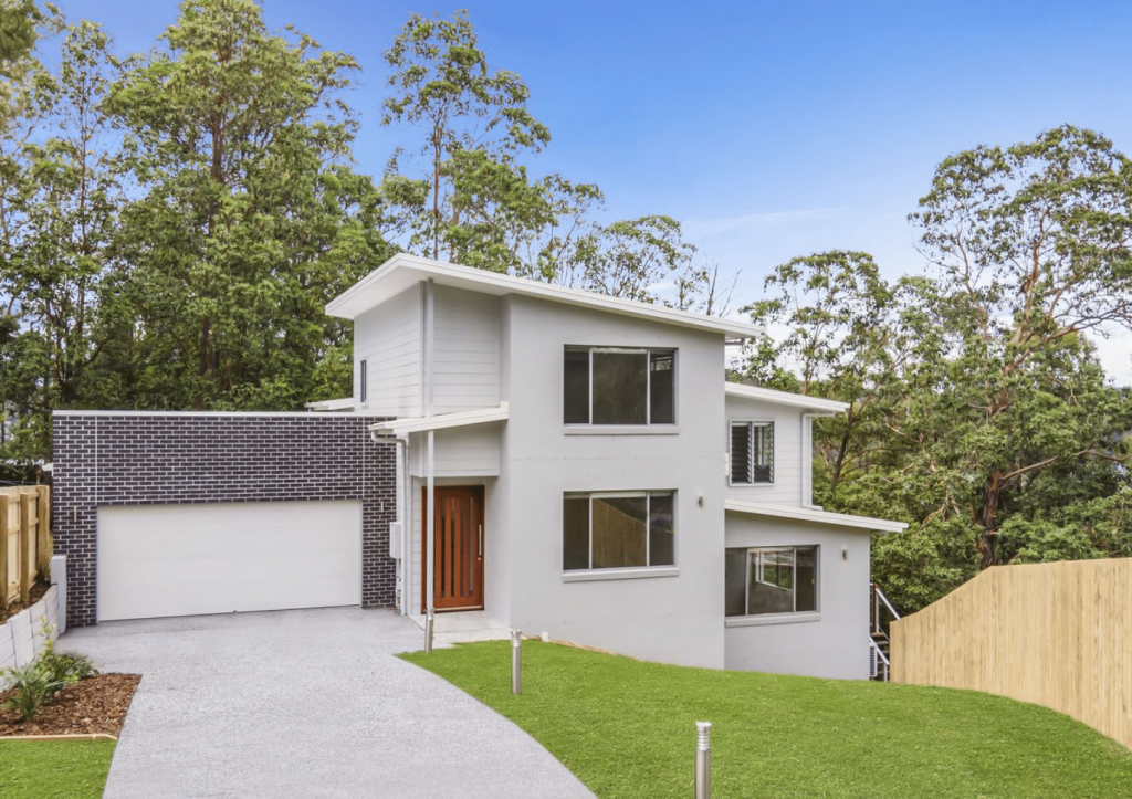 Modern two-story house with a white exterior, dark roof, and attached garage, surrounded by greenery.