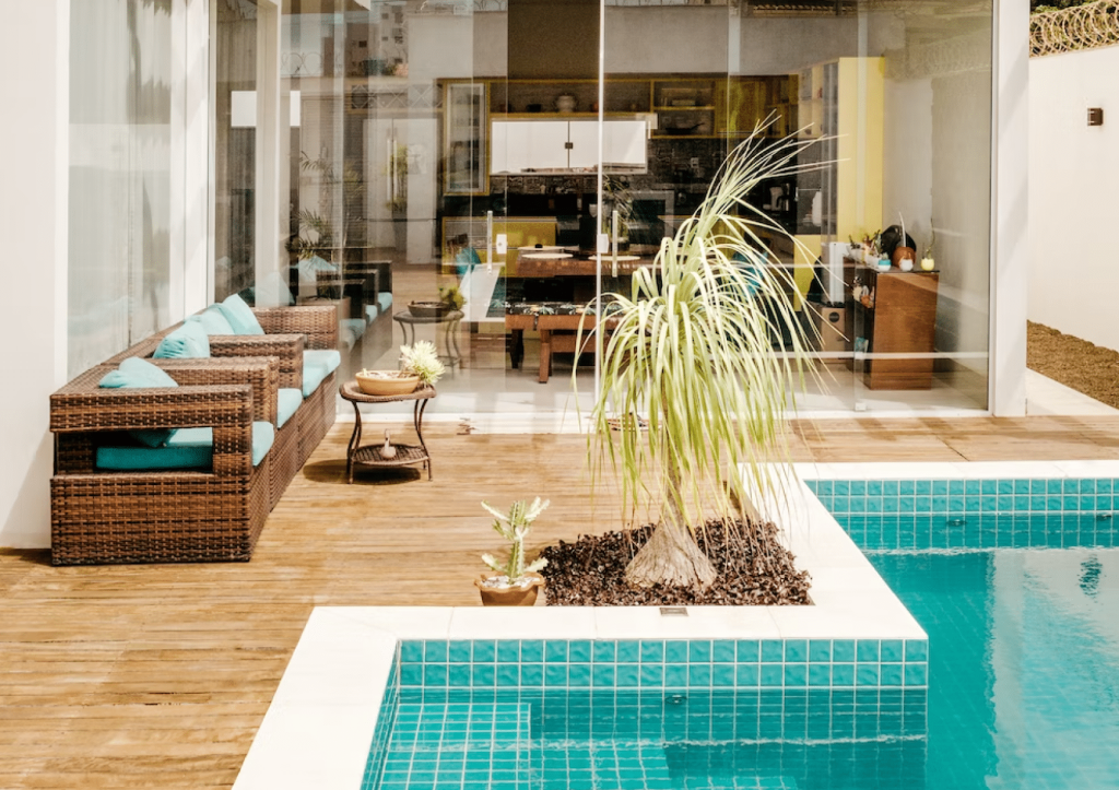 Modern outdoor patio seamlessly blending with an indoor kitchen area, featuring wicker furniture and an inviting swimming pool.