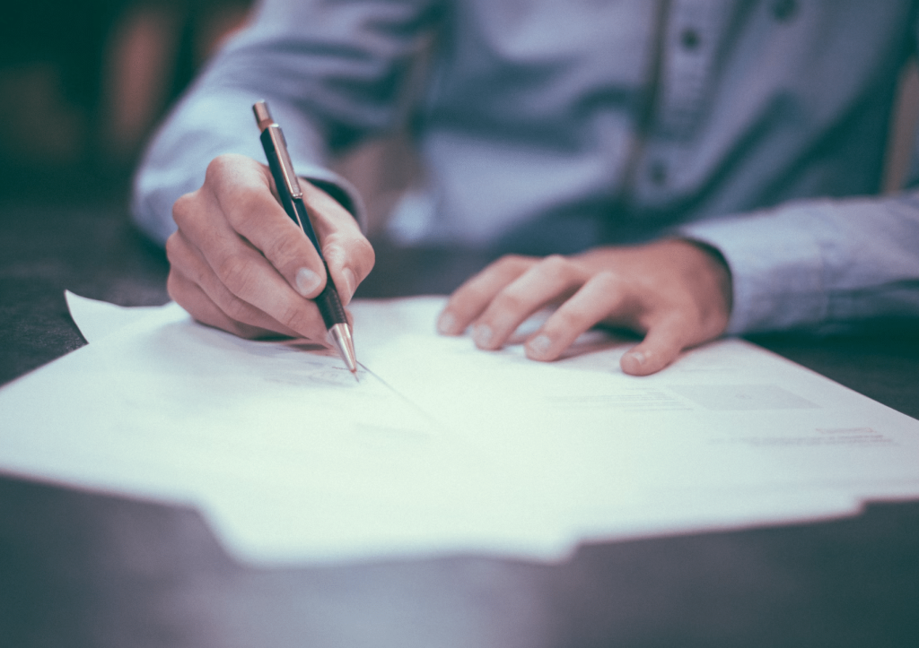 Person signing a document on a wooden table.