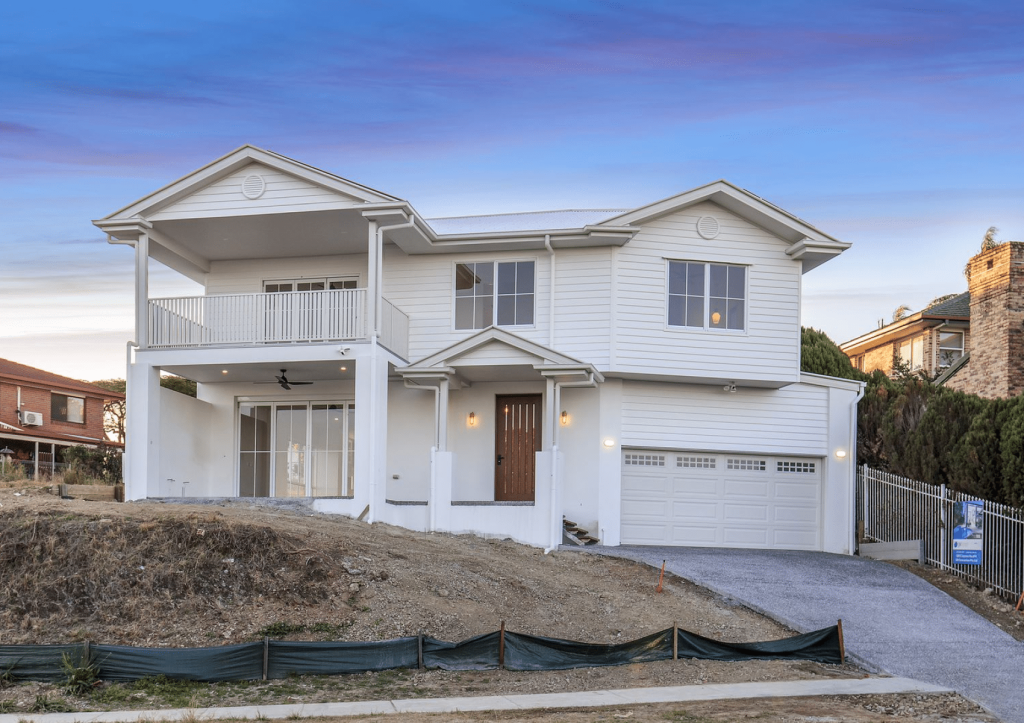 A new two-story house with a white exterior, balcony, and double garage at dusk.