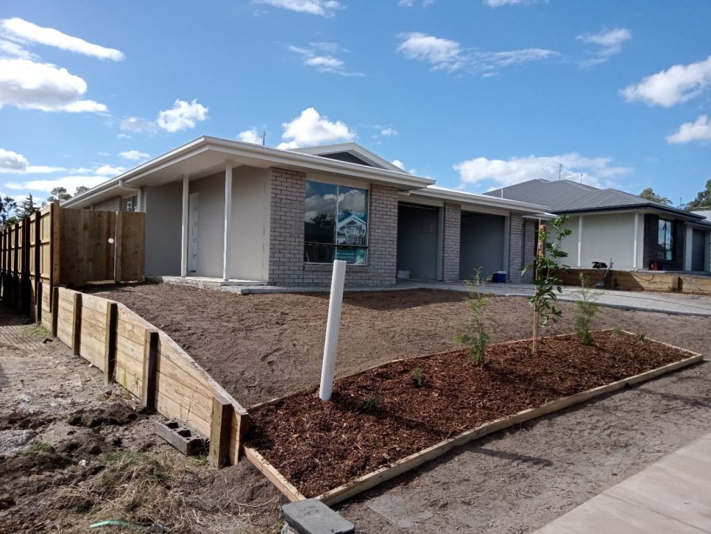 Newly constructed single-story house with an unfinished yard and a real estate sign in front.